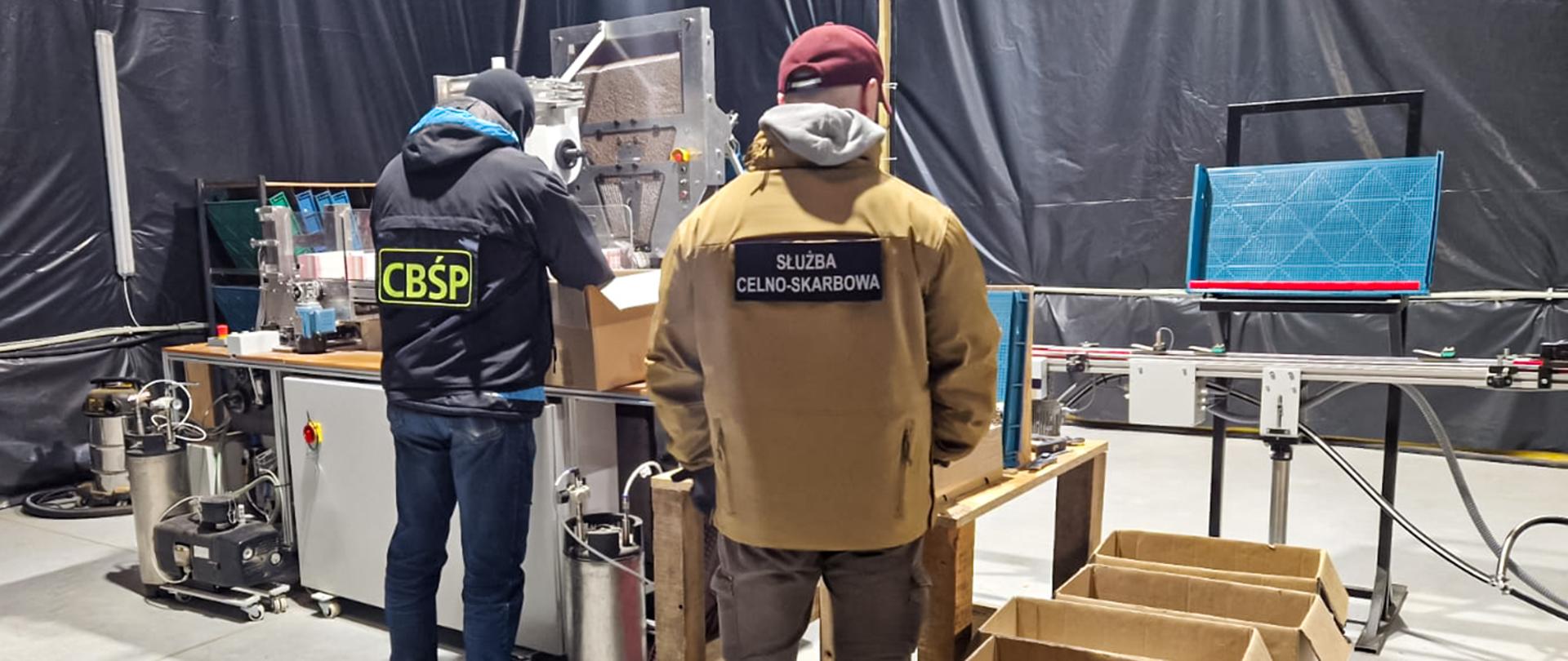 Funkcjonariusze KAS i CBŚP przy maszynie do produkcji papierosów 