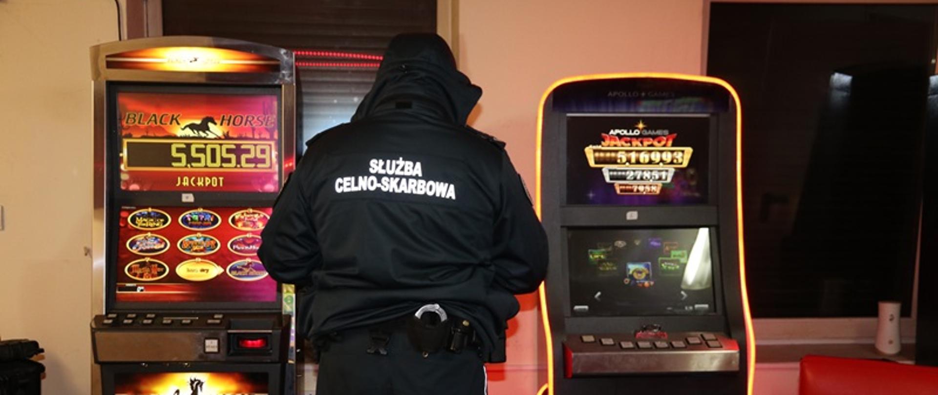 Funkcjonariusz Służby Celno-Skarbowej stoi przed automatami do gier hazardowych. 