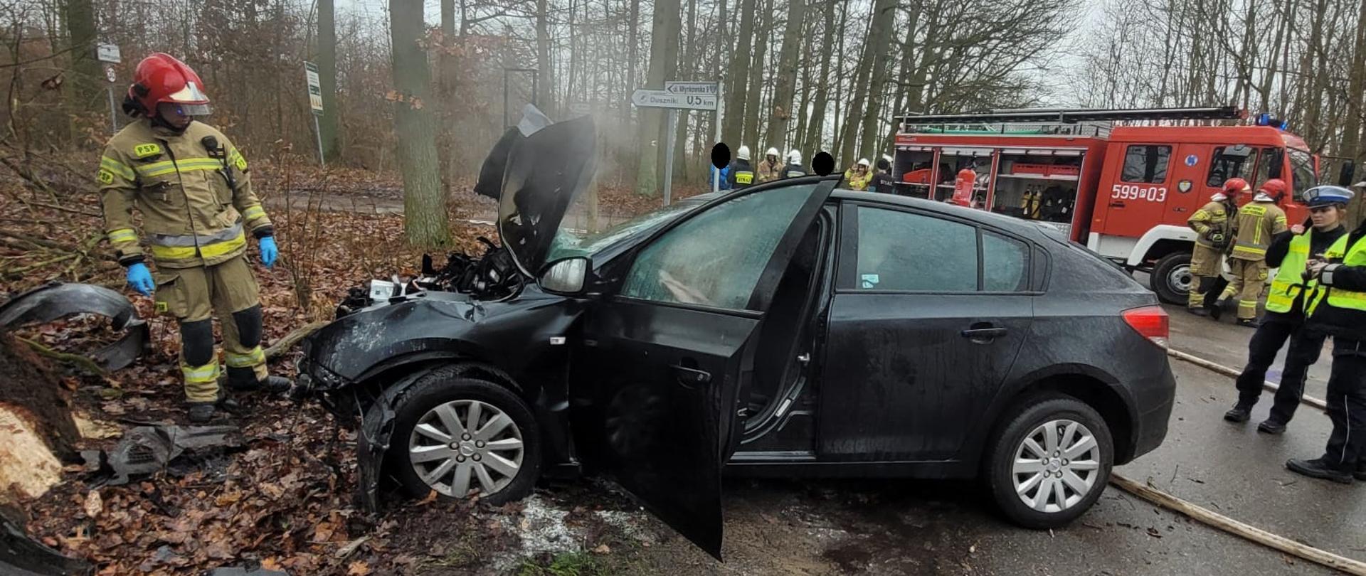 Uszkodzony samochód na drodze, w pobliżu strażacy i policja