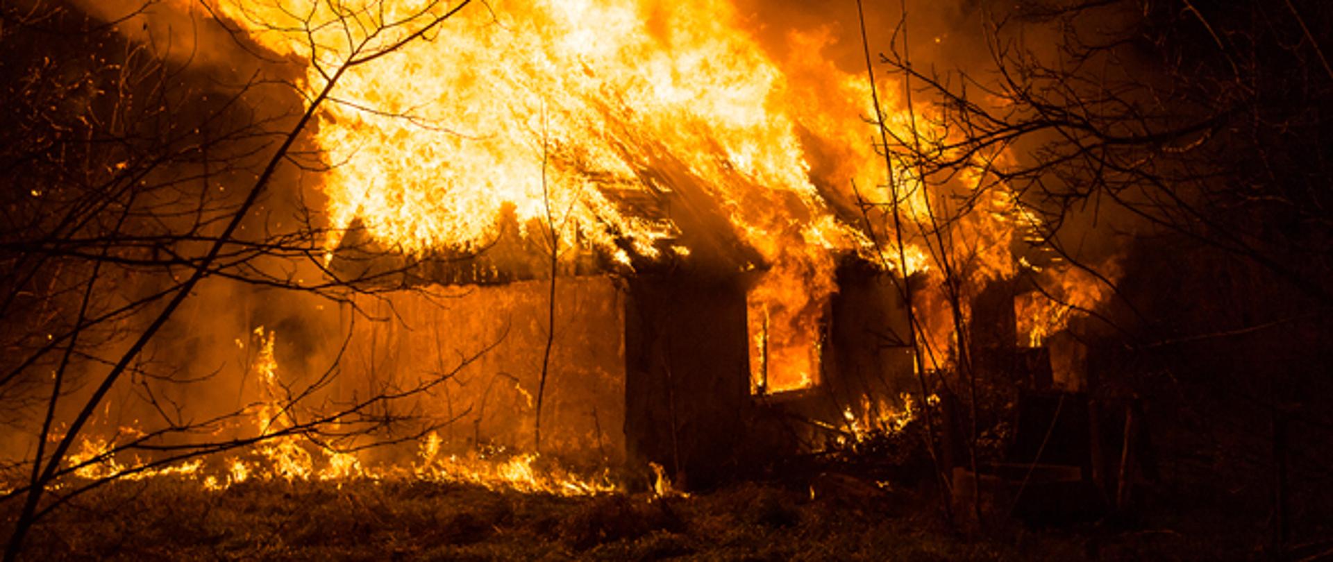 Parterowy budynek w całości objęty pożarem. Zdjęcie wykonane w porze nocnej.