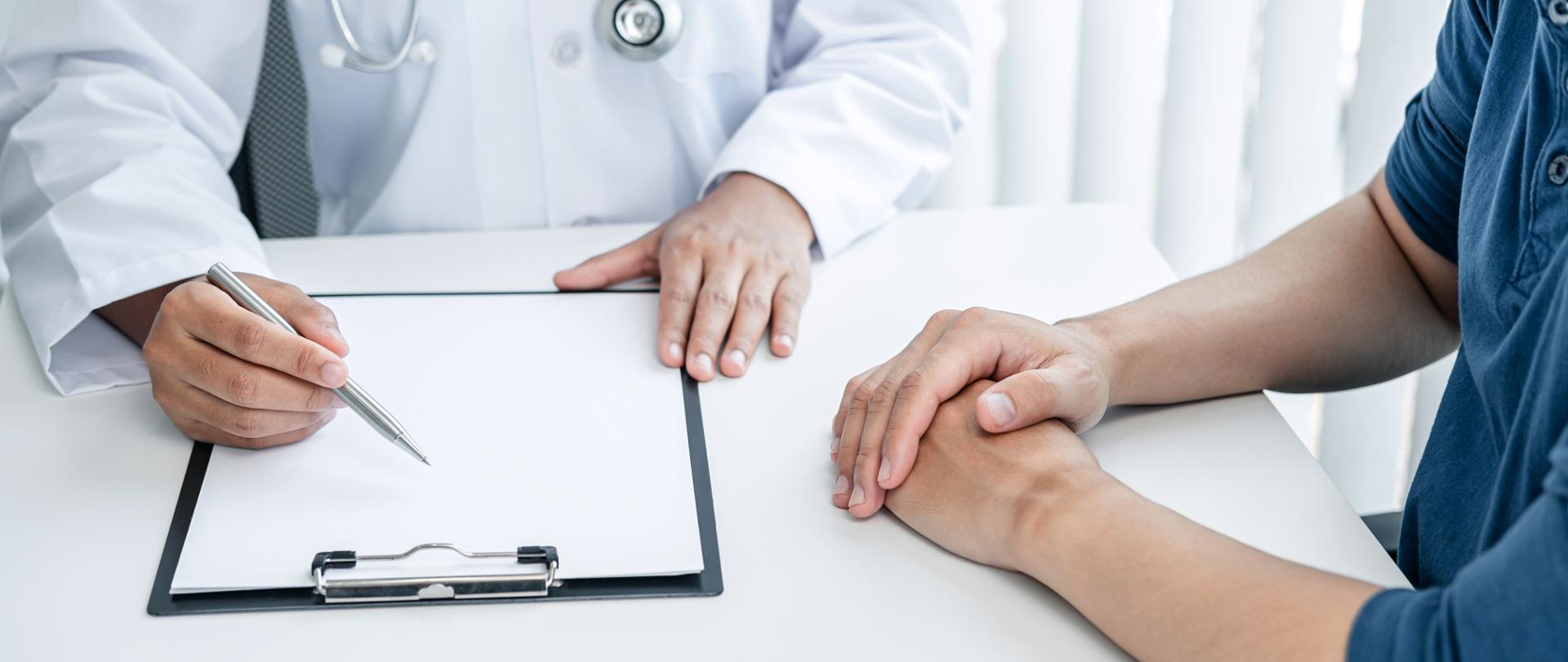 widać dłonie pacjenta i dłonie lekarza robiącego notatki