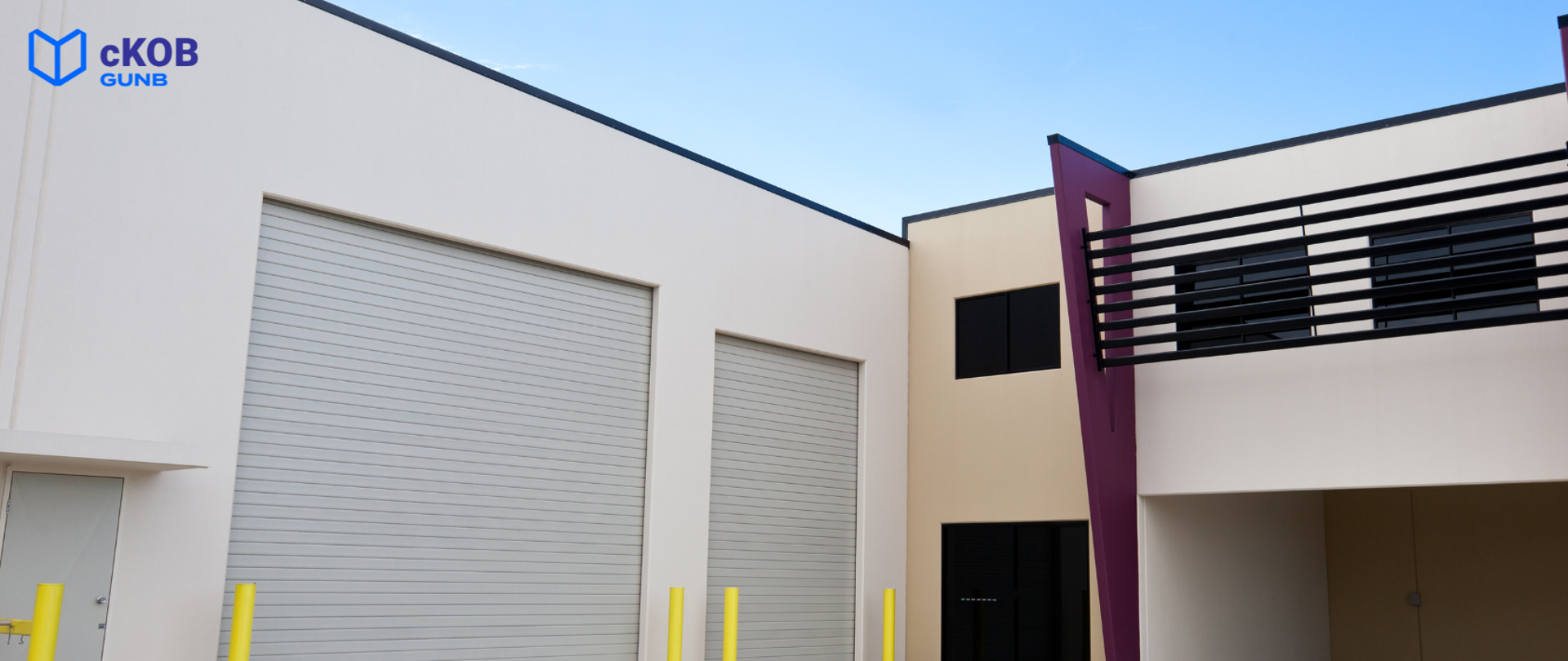 Budynek z bramami i piętrem z balustradami, w kolorach bieli, beżu i fioletu, z logo „cKOB GUNB”.