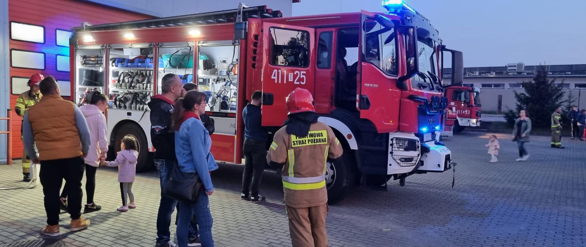 Na zdjęciu goście odwiedzający Komendę Powiatową PSP w Jędrzejowie podczas Jędrzejowskiej Nocy Muzeów. Na zdjęciu widnieje też strażak w umundurowaniu bojowym oraz samochód ratowniczo-gaśniczy. 