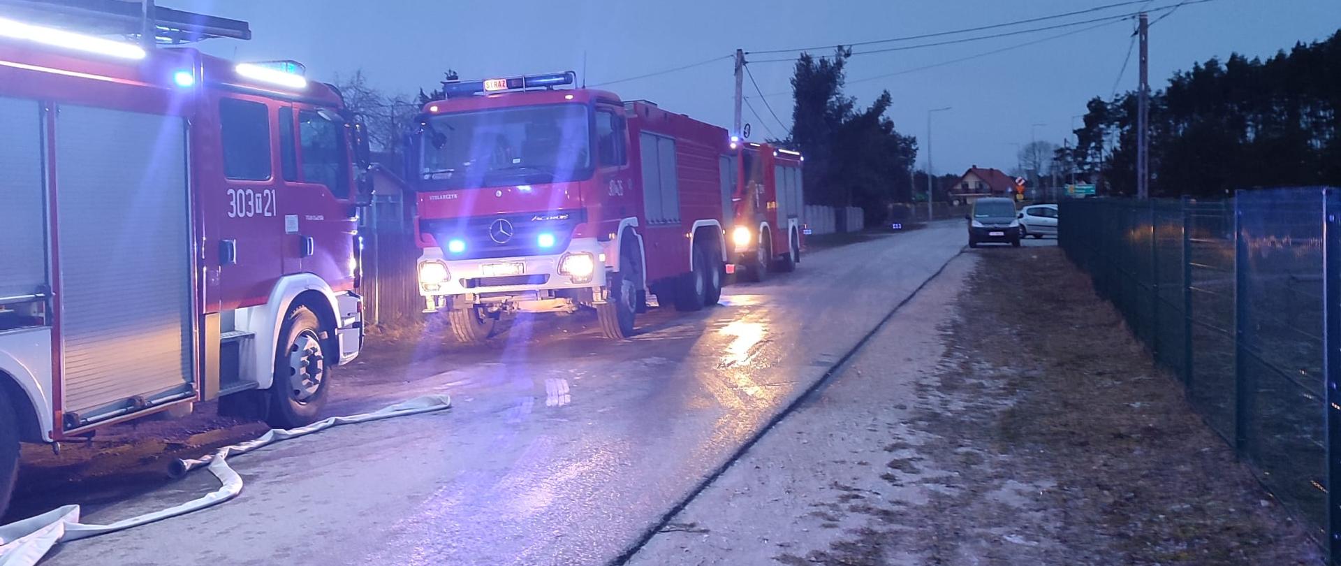 Zdjęcie przedstawia ulicę Wymysłów. Po lewej stronie, na jezdni stoją trzy samochody pożarnicze oraz widać rozwinięte węże gaśnicze.