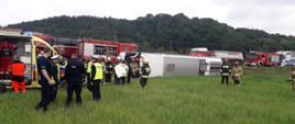 Na zdjęciu widoczny przewrócony autobus obok na drodze widoczne samochody ratowniczo-gaśnicze straży pożarnej oraz funkcjonariusze straży pożarnej i Policji.