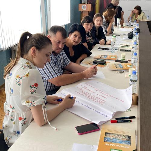 Grupa 11 osób przy stole konferencyjnym notuje coś na dużych kartkach papieru.