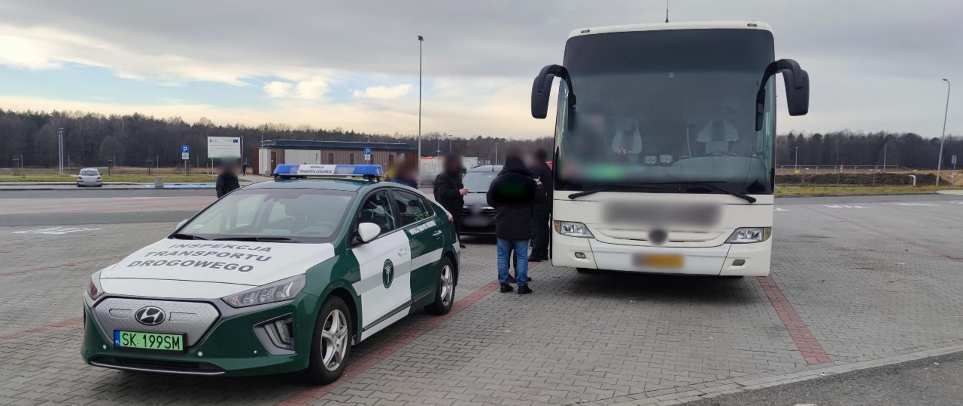 Od lewej: oznakowany radiowóz śląskiej Inspekcji Transportu Drogowego o napędzie elektrycznym i zatrzymany do kontroli autobus dalekobieżny stoją na parkingu koło autostrady A1.