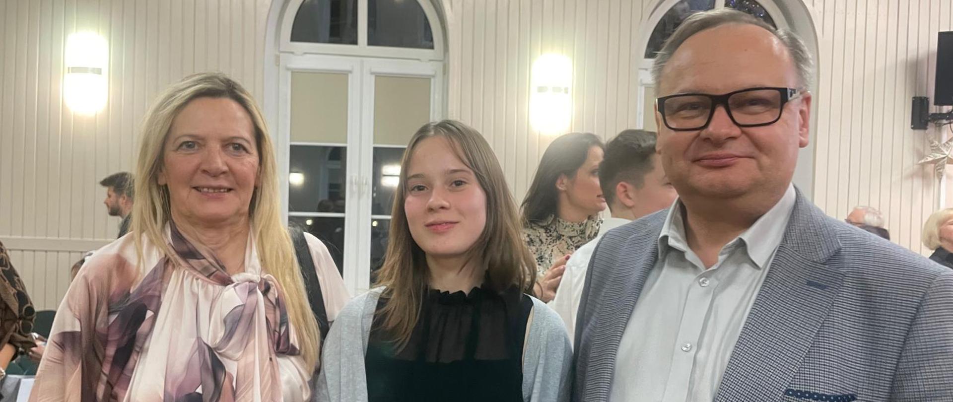 Na zdjęciu pozuje Anna Łysko wraz z uczennicą Kingą Basendowską oraz Grzegorzem Wieczorkiem. Wszyscy uśmiechnięci.