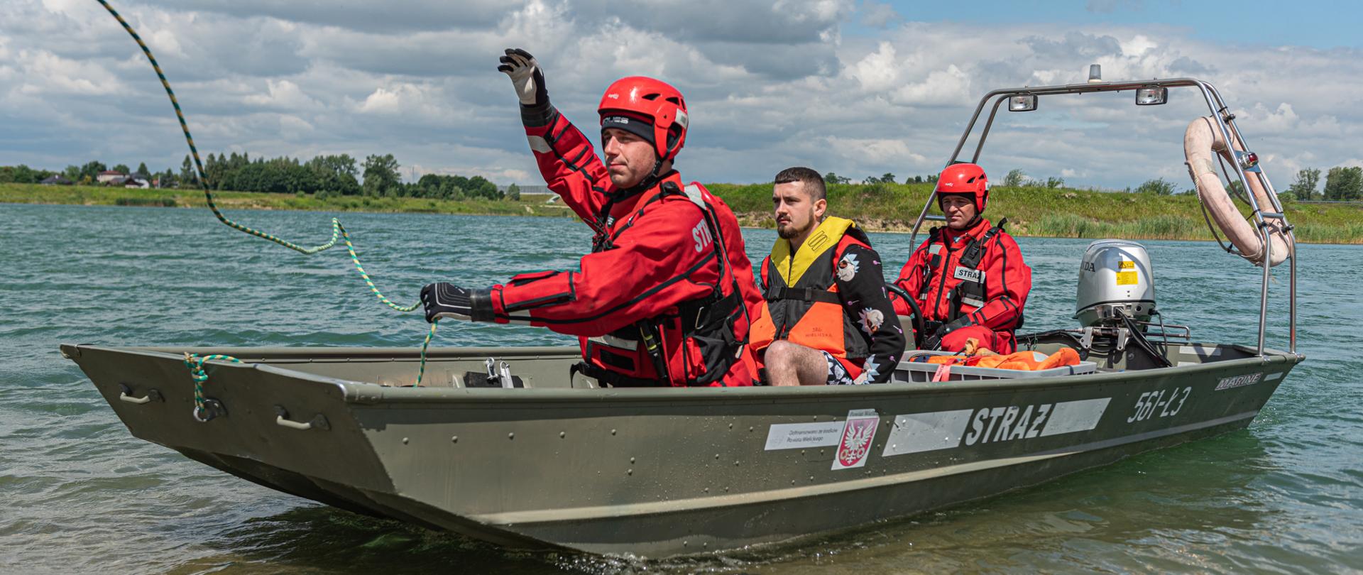 Na zdjęciu dwóch strażaków w łodzi dopływających do brzegu. W łodzi również znajduje się jedna osoba w kamizelce ratunkowej.
