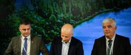 Deputy Minister Mikołaj Dorożała signs the Forest Europe Ministerial Declaration on 2 June 2026. In the photo, the Deputy Minister is seated at a table signing the document. Two men are seated beside him, one on each side. A forest-themed graphic can be seen in the background.
