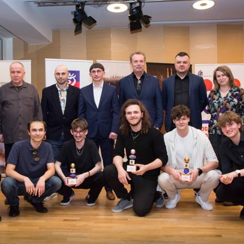 Zdjęcie przedstawia jurorów konkursu oraz laureatów starszej grupy konkursu we wspólnym zdjęciu na scenie sali koncertowej, w tle banery sponsorów i szkoły