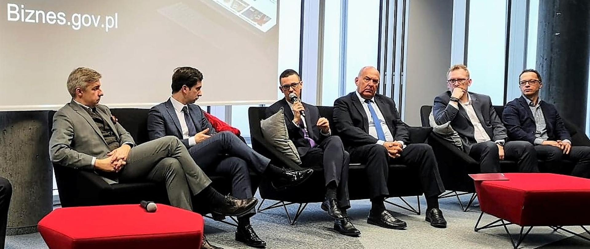 Paneliści siedzą na kanapach. Wśród nich wiceminister Karol Okoński.