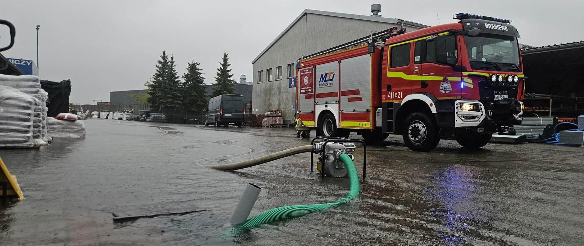 Zdjęcie obrazujące zalaną ulice miasta, strażacy wypompowują wodę, w tle samochód strażacki