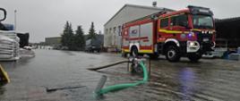 Zdjęcie obrazujące zalaną ulice miasta, strażacy wypompowują wodę, w tle samochód strażacki