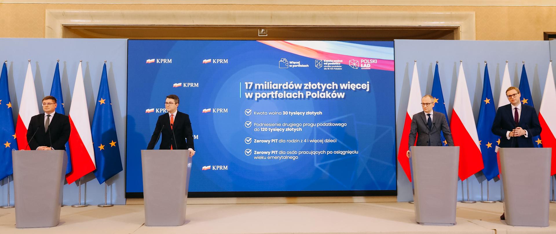 Konferencja z udziałem wiceministra Tomasza Rzymkowskiego dotycząca wynagrodzeń dla nauczycieli w Polskim Ładzie, wiceminister Tomasz Rzymkowski w pozostałymi uczestnikami konferencji stoi na scenie przed mikrofonem.