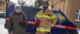 Zdjęcie przedstawia seniora oraz strażaka Ochotniczej Straży Pożarnej w Kiwitach przed przychodnia, gdzie wykonuję się szczepienia. W tle znajduje się samochód gospodarczy z OSP.