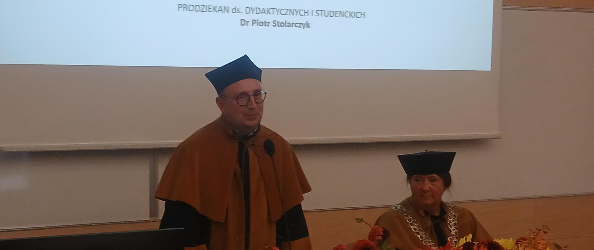 dwóch pracowników w oficjalnych strojach na tle planszy