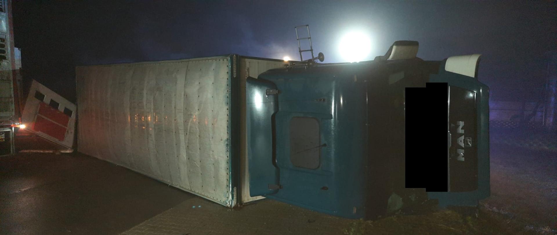 Widać przewrócony samochód ciężarowy na drodze, jest ciemno