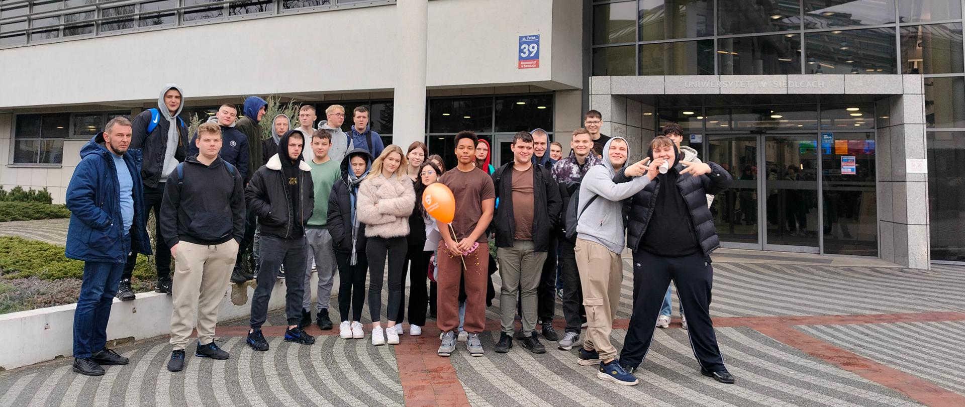 Grupa uczniów stoi przed budynkiem głównym Uniwersytetu w Siedlcach