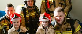 Dzieci przebrane w strój strażaka pozują razem ze strażakami.