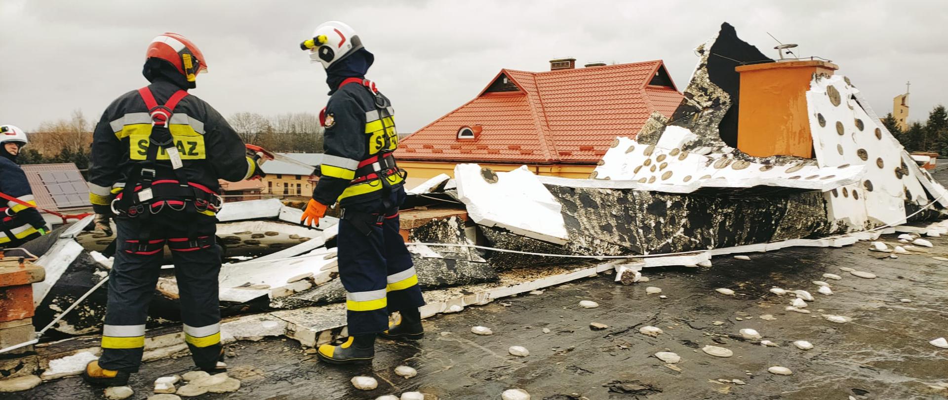 Na zdjęciu widzimy strażaków na stropodachu budynku szkoły zabezpieczających zerwane poszycie dachu.