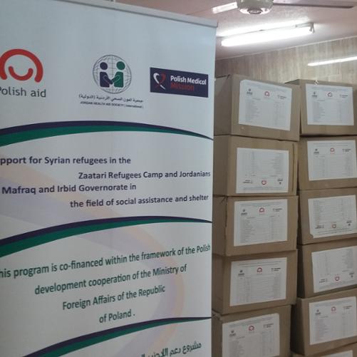 w magazynie stoją pudełka oznaczone logo Polska pomoc. Obok pudełek stoi rollup z napisem projektu