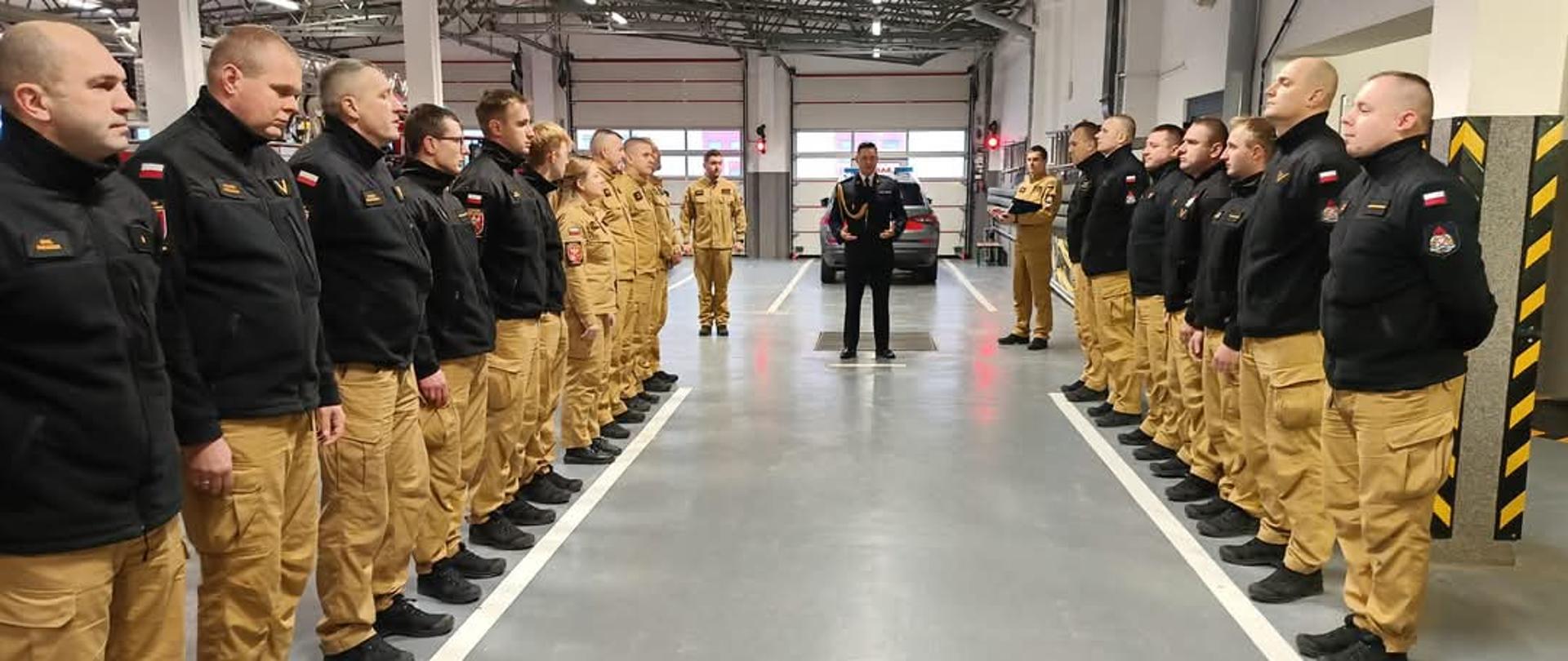 Zbiórka strażaków w garażu. Na zdjęciu widać stojących strażaków w ubraniach służbowych. 