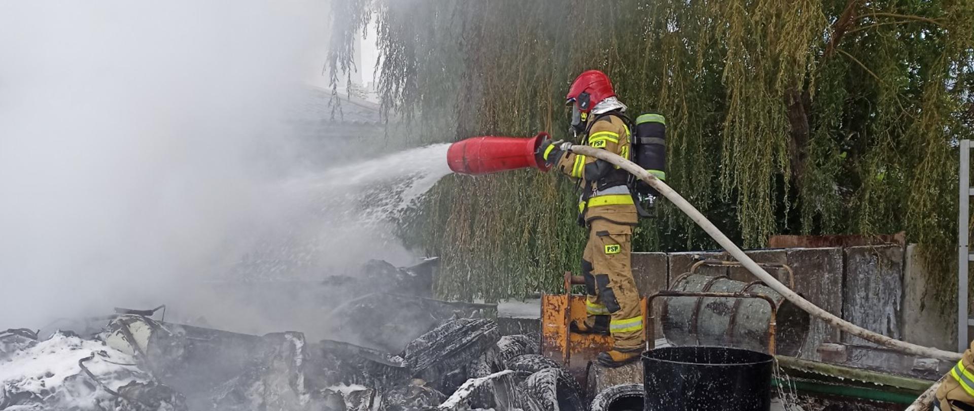 Zdjęcie przedstawia strażaka gaszącego pryzmę elementów demontażu aut