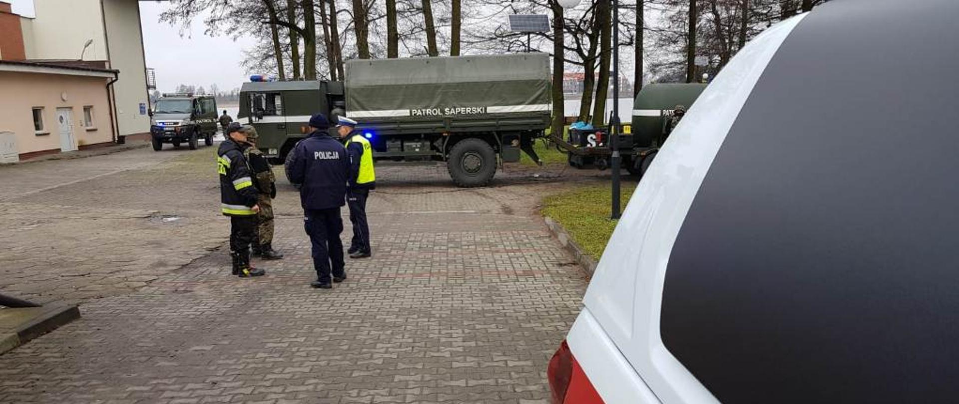 Na tle samochodu wojskowego patrolu saperskiego widać rozmawiających pracowników policji w Ostródzie, żołnierza wojskowego patrolu saperskiego oraz st. kpt. Marcina Wiśniewskiego. 