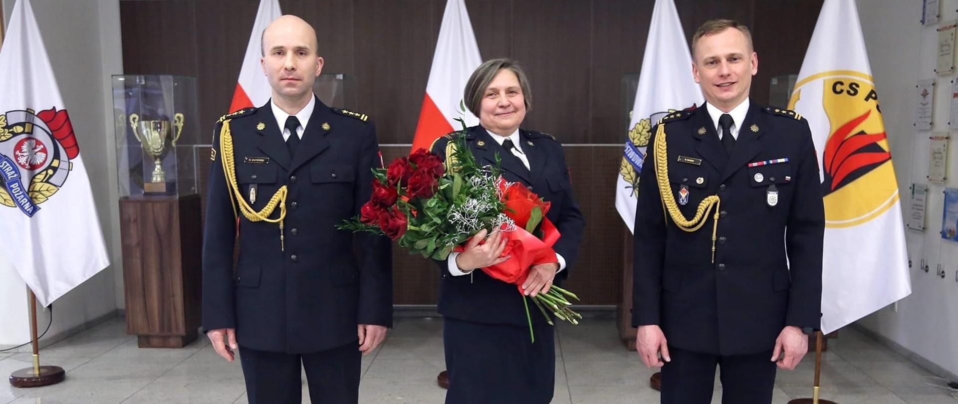 Na zdjęciu odchodząca na emeryturę Pani brygadier, trzymająca bukiet czerwonych róż w towarzystwie obu Zastępców Komendanta Centralnej Szkoły PSP
