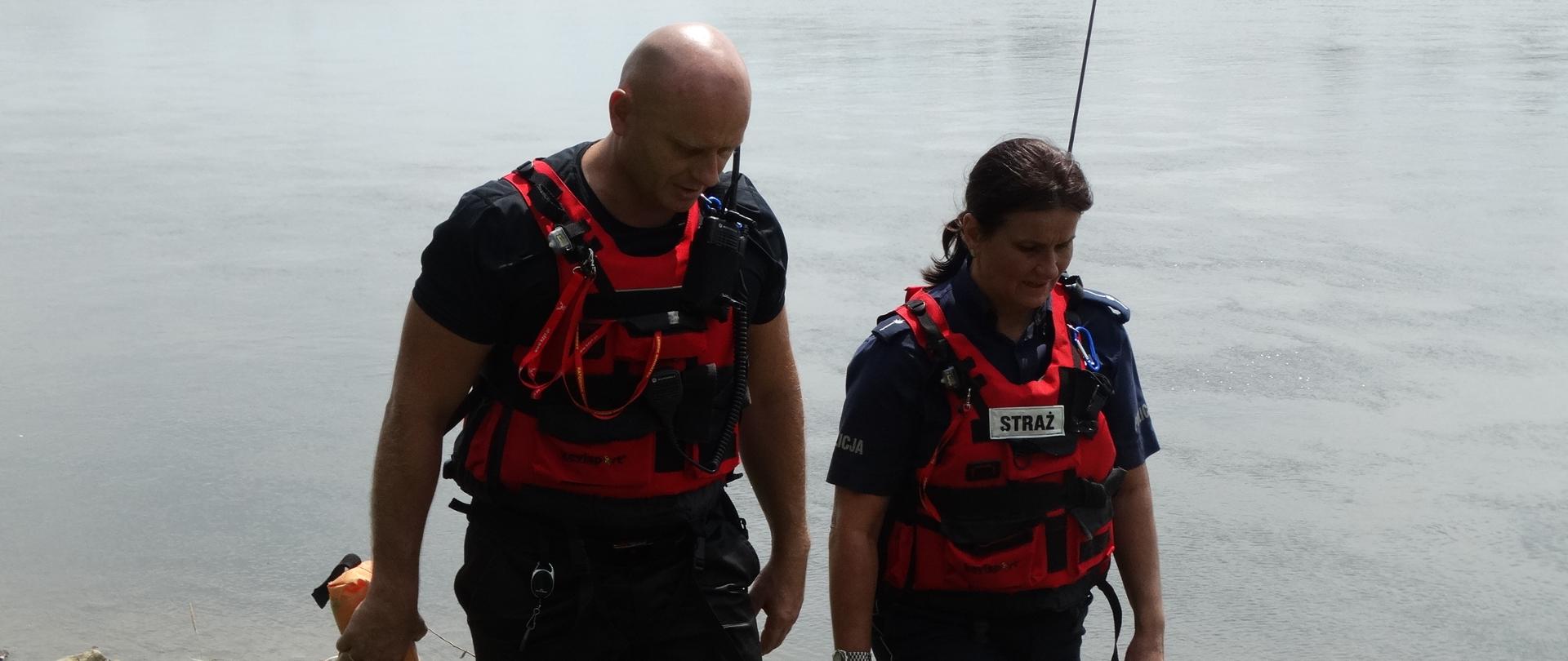 Dwie osoby wspólnie patrolują akwen wodny. Ubrani są w kamizelki.