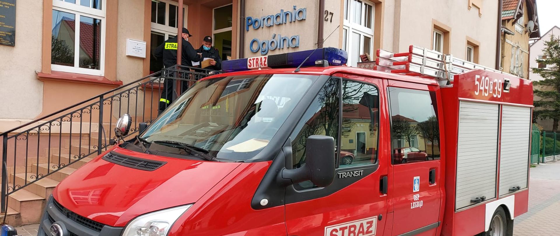 Na zdjęciu widać samochód strażacki z jednostki Ochotniczej Straży Pożarnej w Legbądzie. W tle widoczny jest budynek Miejskiego Centrum Lekarskiego w Tucholi, natomiast przed wejściem do budynku stoją druhowie z jednostki Ochotniczej Straży Pożarnej w Legbądzie (w umundurowaniu koszarowym).