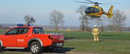 Z doraźnego miejsca lądowania przygotowanego na łące, startuje śmigłowiec LPR. Start zabezpiecza dwóch strażaków w ubraniach specjalnych koloru piaskowego oraz w białych hełmach. Na pierwszym planie terenowy samochód straży pożarnej. na jego tylnych drzwiach widnieje numer operacyjny 571P92, a na tylnej klapie - napis STRAŻ.