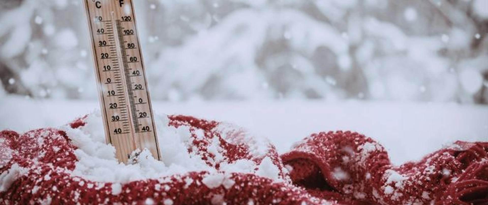 termometr owinięty szalikiem w śniegu, pokazujący ujemną temperaturę