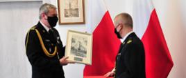 Zdjęcie przedstawia pomorskiego komendanta wojewódzkiego PSP st. bryg. Piotra Sochę wręczającego pamiątkowy obraz mł. bryg. Waldemarowi Lewandowskiemu.