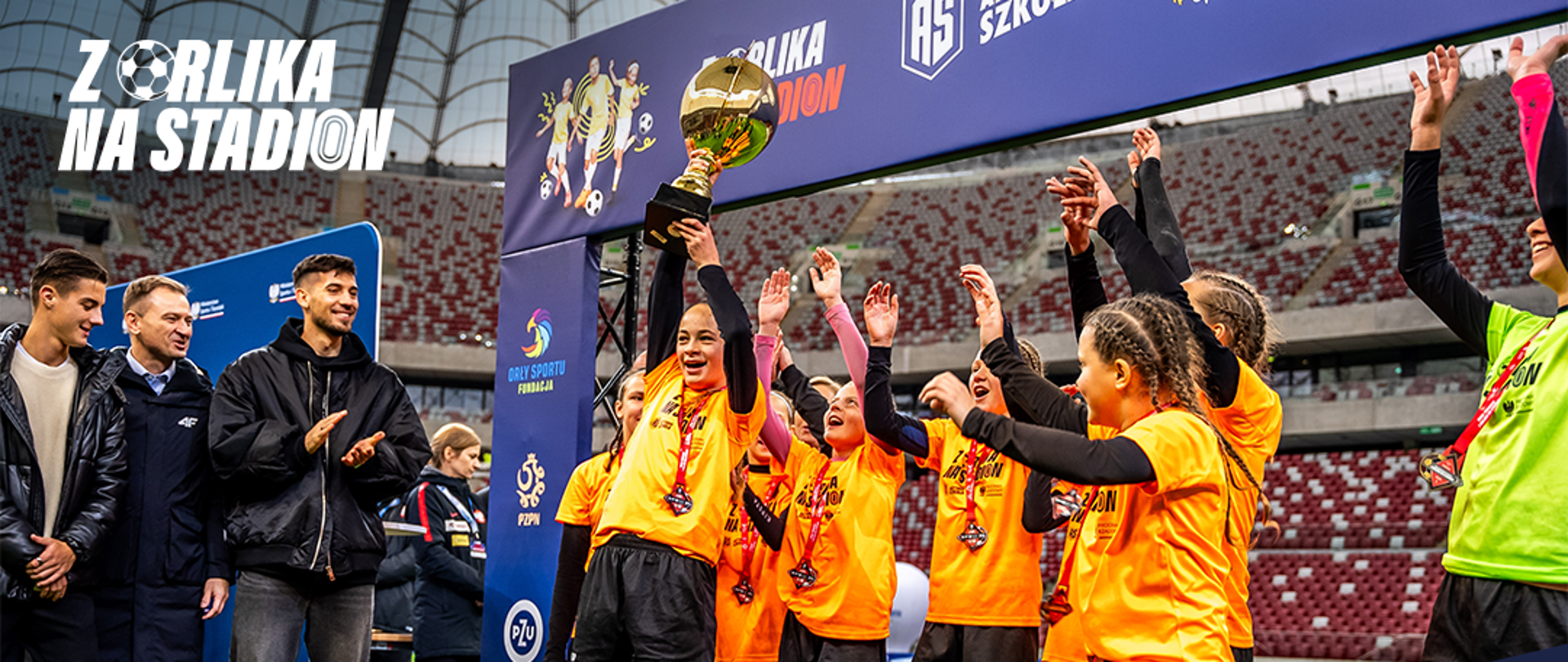 Grafika z napisem w lewym górnym rogu: "Z Orlika na Stadion". Poniżej zdjęcie z finałów ogólnopolskich pierwszej edycji turnieju, rozgrywanych na PGE Narodowym. Na zdjęciu od lewej stoją: Kacper Urbański, Minister Sportu i Turystyki Sławomir Nitras i Jakub Moder, drużyna dziewcząt, która odebrała puchar za zwycięstwo. Niżej duży napis na granatowym tle: "Rekrutacja drużyn do II edycji ogólnopolskiego turnieju Z Orlika na Stadion. Weź udział w eliminacjach: www.zorlikanastadion.pl". Na samym dole biały pasek z logotypami: Program Rządowy, MSiT, MEN, Aktywna Szkoła i Fundacja Orły Sportu.