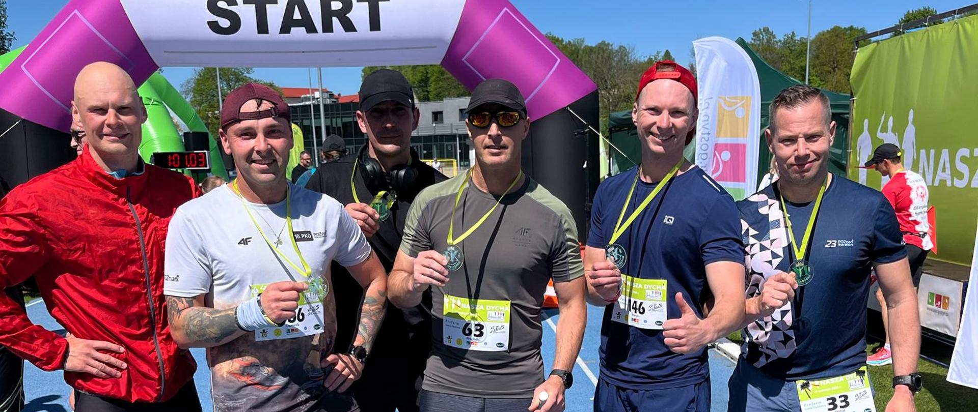 Strażacy stoją z medalami na bieżni. Są po biegu.