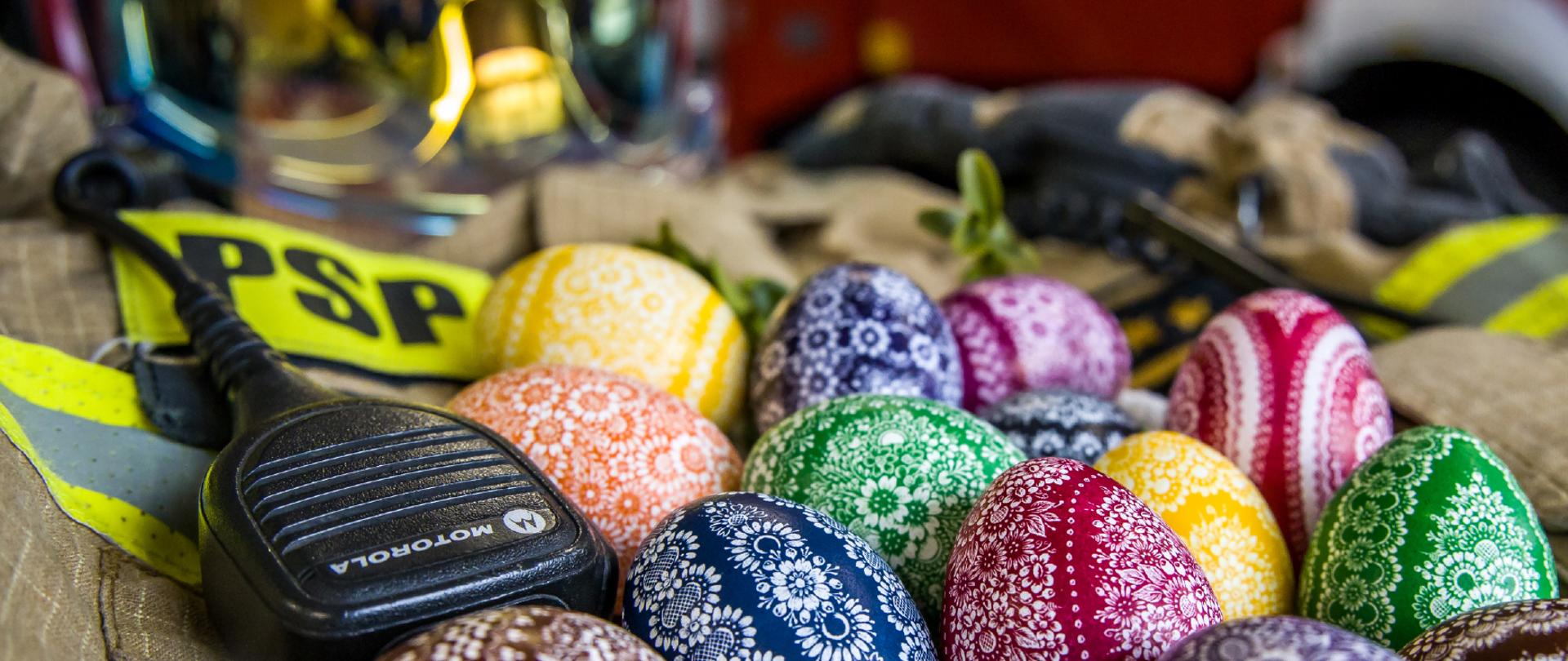 Życzenia Świąteczne Opolskiego Komendanta Wojewódzkiego PSP z okazji Świąt Wielkanocnych. Na górnej części kroszonki leżące na kurtce munduru bojowego na tle hełmu i pojazdu pożarniczego. Treść: Z okazji zbliżających się Świąt Wielkanocnych życzę Państwu niezapomnianych chwil refleksji i radości, spędzonych wspólnie przy rodzinnym stole. Niech Wielkanocny czas odrodzi wszystko, co dobre, przegoni troski i smutki. Niech obudzi w nas nadzieję na lepsze jutro, ale też sprawi abyśmy byli wdzięczni za to, co już nam dane. Życzę aby tegoroczne Święta Wielkiej Nocy stały się dla nas wszystkich okazją do pojednania i okazywania sobie wsparcia, tolerancji oraz szacunku. Niech Zmartwychwstały Chrystus otacza nas łaską, błogosławi nam wiarą, nadzieją i miłością.