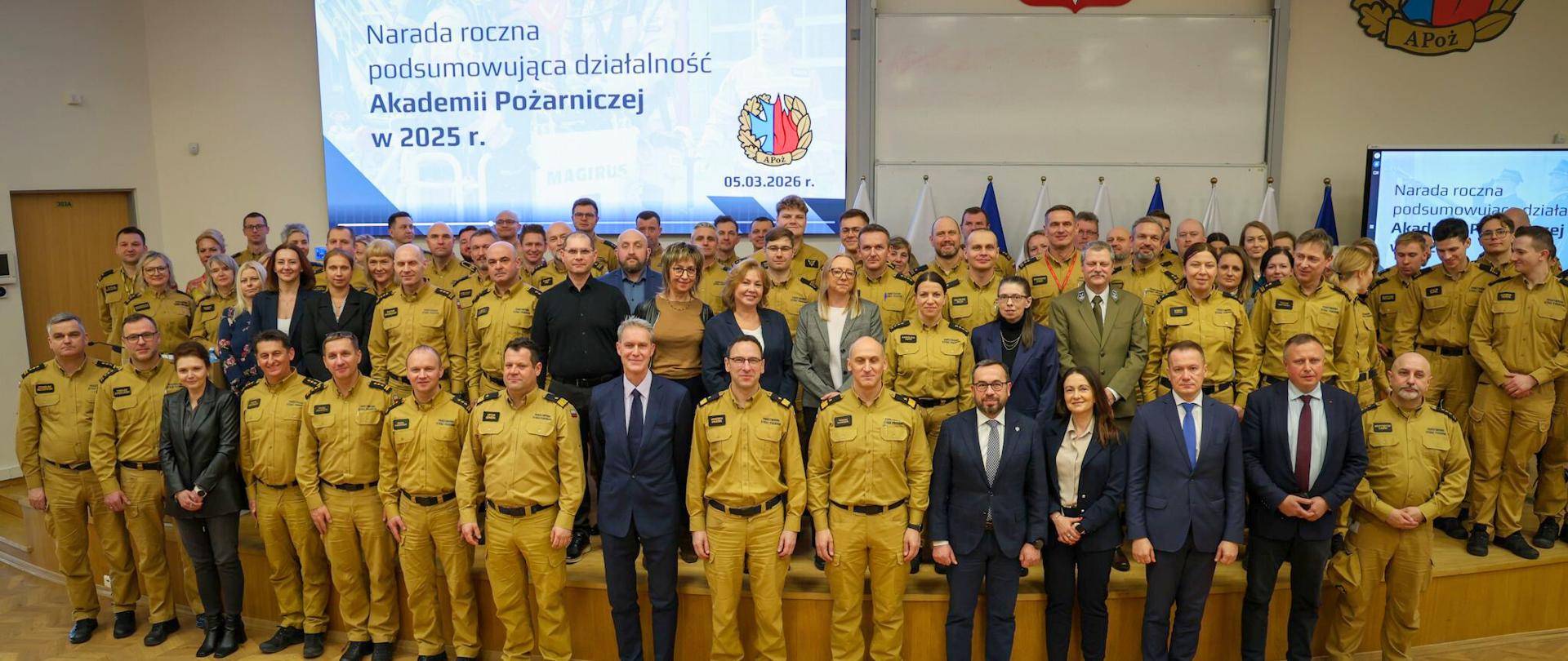Uczestnicy narady rocznej Akademii Pożarniczej – strażacy PSP oraz zaproszeni goście – stoją razem do wspólnego zdjęcia w auli uczelni.