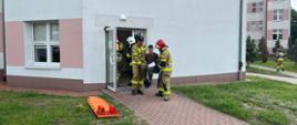 Strażacy ewakuują poszkodowanego na krześle. Osoba z ograniczeniami ruchomości.