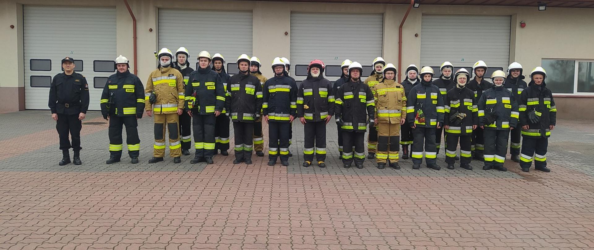 Ceremonia zakończenia szkolenia. Strażacy ustawieni w szyku. W tle budynek Komendy.