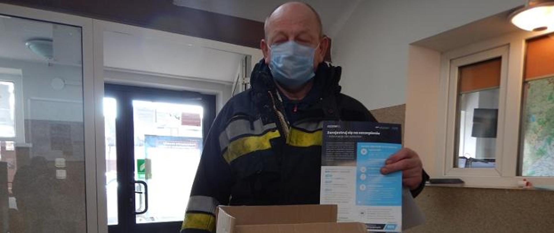 strażak w maseczce ochronnej pokazuje ulotkę 