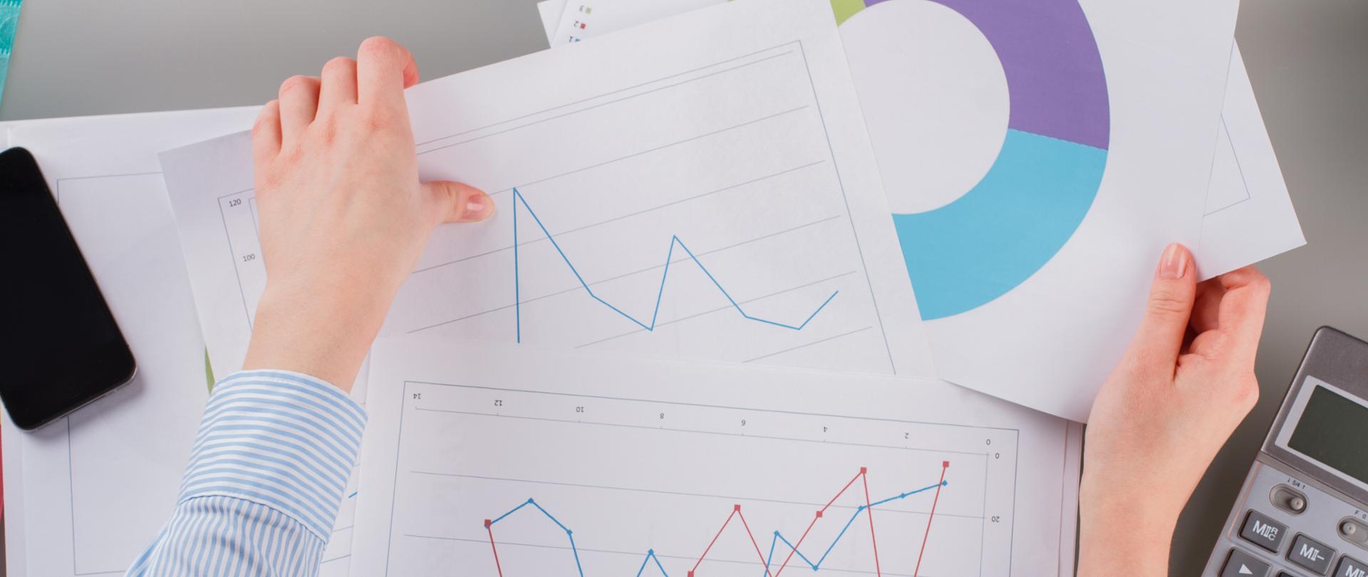 Trader woman working at office close up. Hands of business woman holding graphs while sitting at table in office.