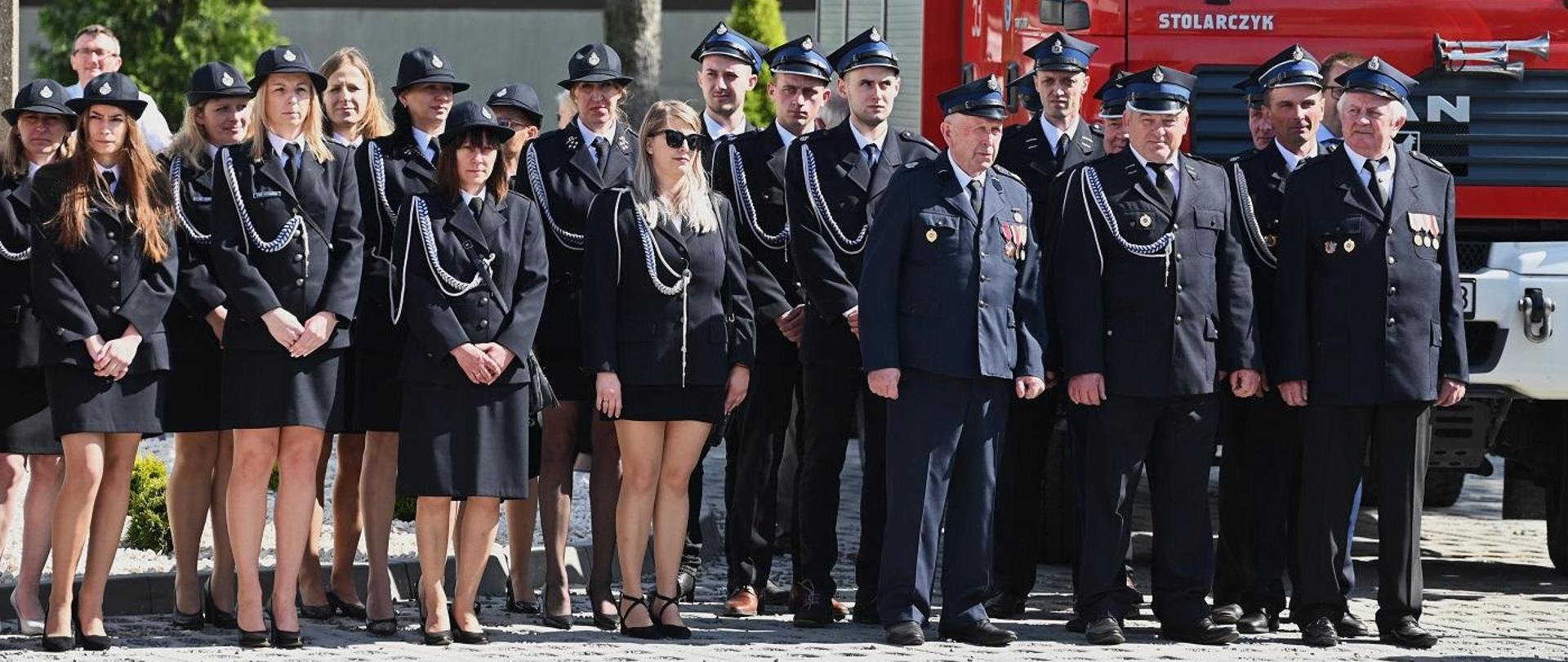 druhowie osp stojący na zbiórce za nimi samochód ratowniczo-gaśniczy