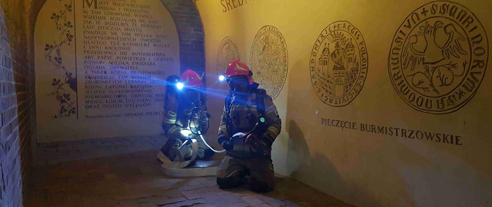 Zdjęcie zrobione w podziemnej części trasy podziemnej. Na zdjęciu wiadać strażaków i linię gaśniczą. 