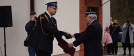 Komendant powiatowy w mundurze galowym wręcza akt włączenia OSP Boreczek do KSRG Prezesowi OSP Boreczek , strażacy w mundurach galowych, w tle remiza OSP