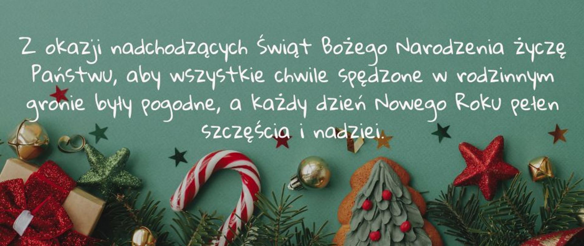 Kartka z życzeniami z okazji Świąt Bożego Narodzenia. Na zielonym tle treść życzeń w kolorze białym. na dole kartki gałązki świerkowe i ozdoby świąteczne: gwiazdki, laski z cukru, pierniczek, złote bombki
