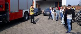 Na zdjęciu znajdują się uczniowie, strażak, samochody osobowe oraz wóz strażacki