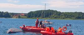 Na zdjęciu widać jak strażacy próbują podnieść żaglówkę by bezpiecznie z holować ją do brzegu. Maszt żaglówki dotyka dna.
