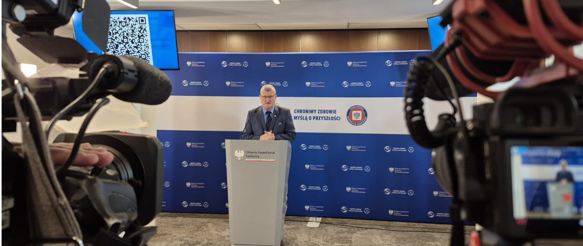Minister Grzesiowski w wystąpieniu prasowym. W tle logo PIS .